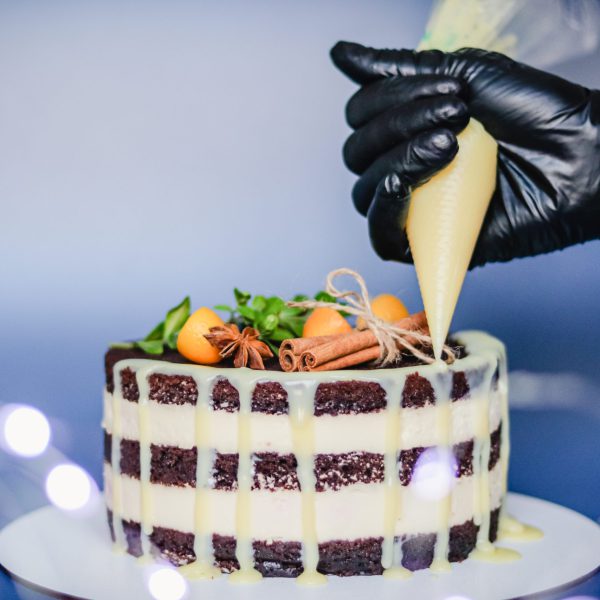 A pastry chef decorates a chocolate naked cake with drips of white chocolate from a pastry bag